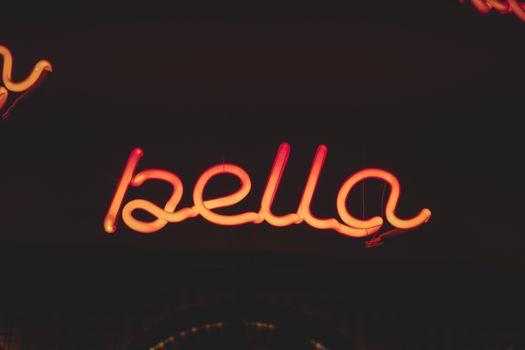 Vibrant neon sign spelling 'bella' glowing against a dark backdrop.