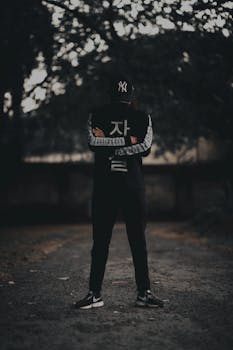 光线昏暗的小路上，一个穿着街头服饰的人站在那里，为场景增添了一丝神秘氛围