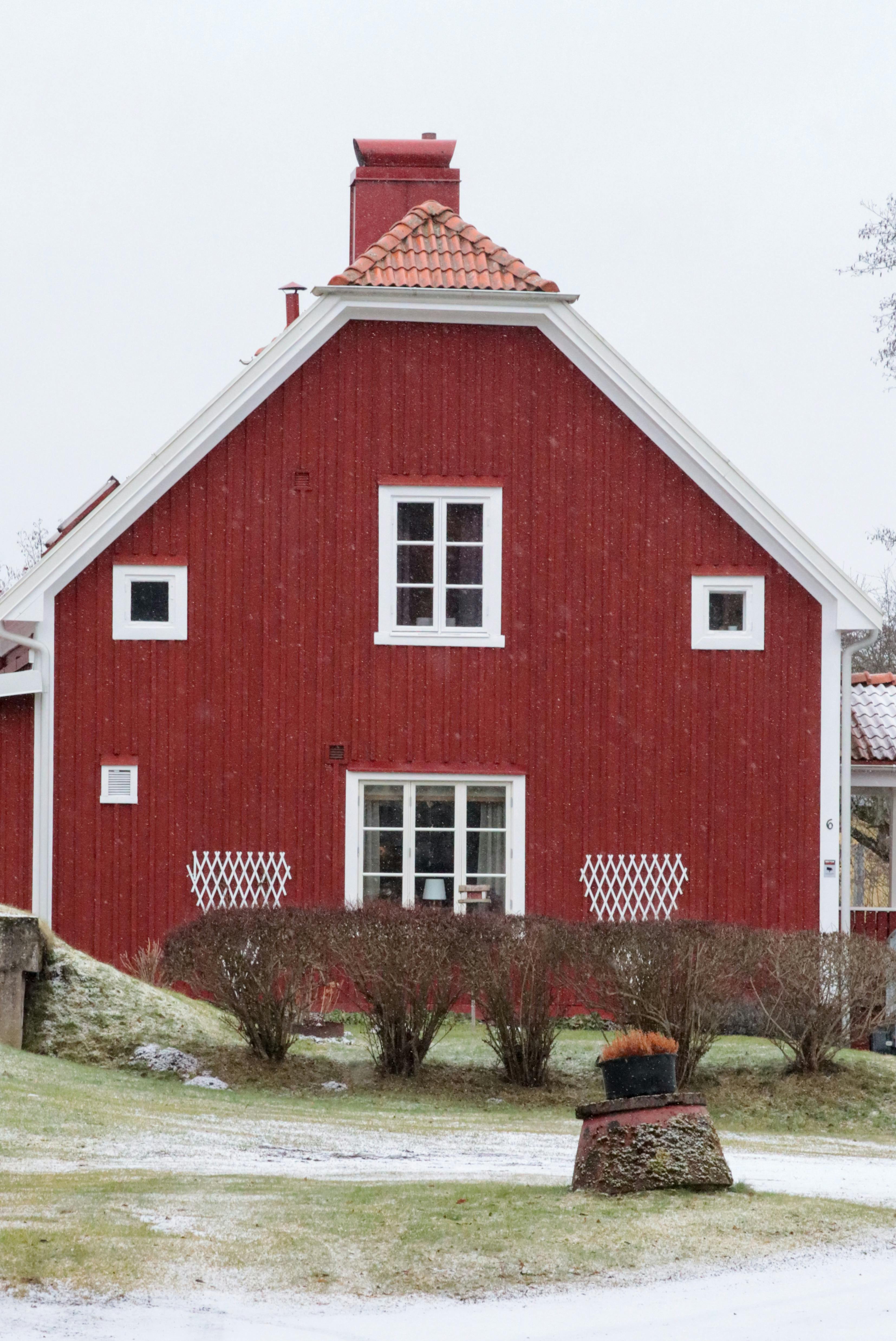 A picturesque red wooden house with a snowy yard in a rural winter setting.