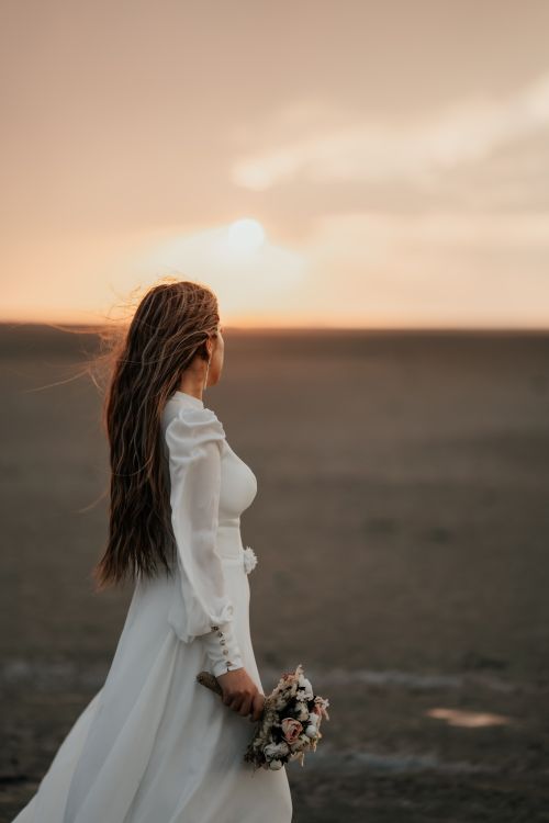 Free A bride holds a bouquet, gazing at the sunset in Tabriz, Iran. Perfect for wedding themes. Stock Photo