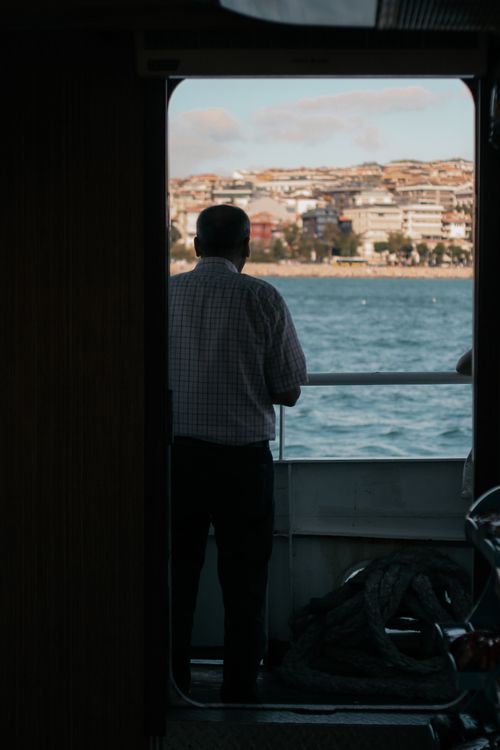 Free A man gazes at the cityscape from a boat deck during sunset, capturing a serene moment. Stock Photo