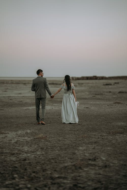Couple Holding Hands and Walking on Wasteland