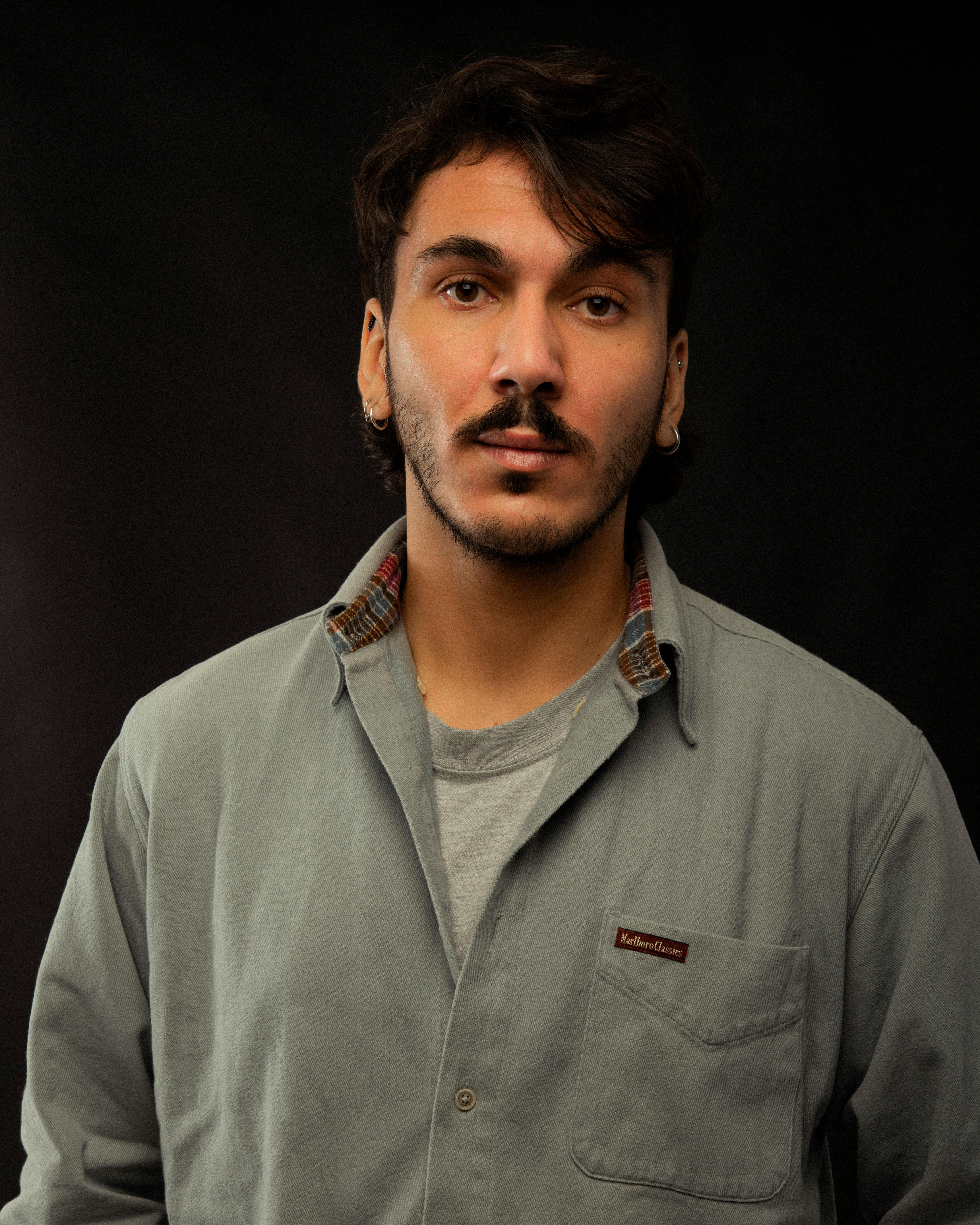 Portrait of a stylish man with a mustache against a dark background, wearing a casual shirt.