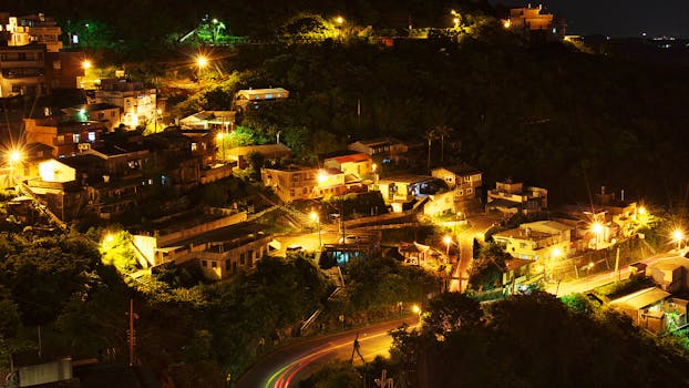 A scenic evening view of a hillside village illuminated by street lights, showcasing urban tranquility.