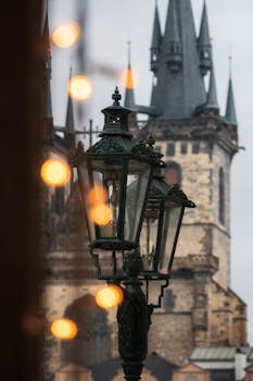 Gothic lanterns with bokeh in front of Prague's famous church tower at twilight.