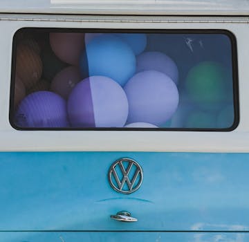 A vibrant blend of balloons fills the rear window of a classic blue van on a sunny day.