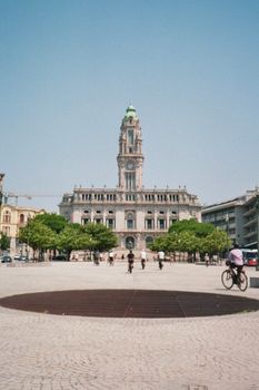 View of Porto City Hall in a lively urban square with cyclists and pedestrians, capturing a sunny day in Porto, Portugal.