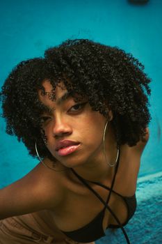 Portrait of a fashionable woman with afro hairstyle and hoop earrings against a vibrant blue background.