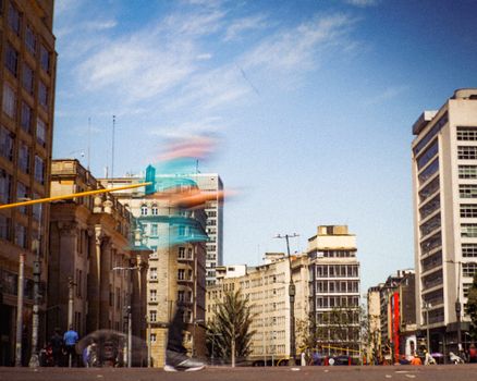 Blurred motion of pedestrians in vibrant Bogotá cityscape under a sunny sky.