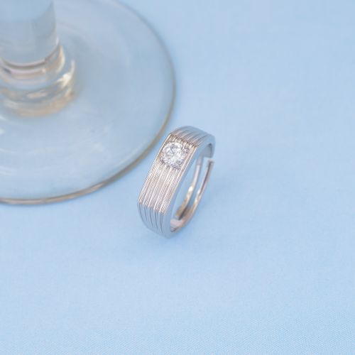 Free Close-up of a textured silver ring with a diamond next to a glass base on a blue surface. Stock Photo