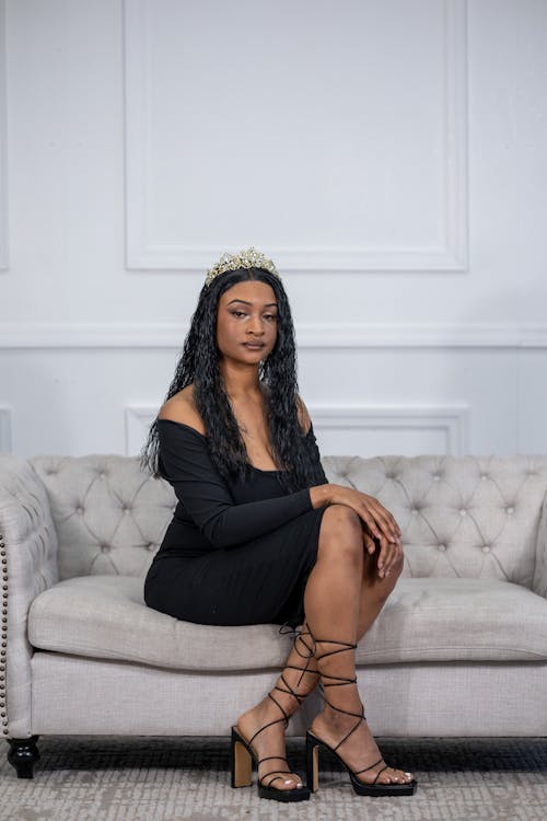 Elegant Woman in a Black Dress and High Heels Sitting on a Sofa 