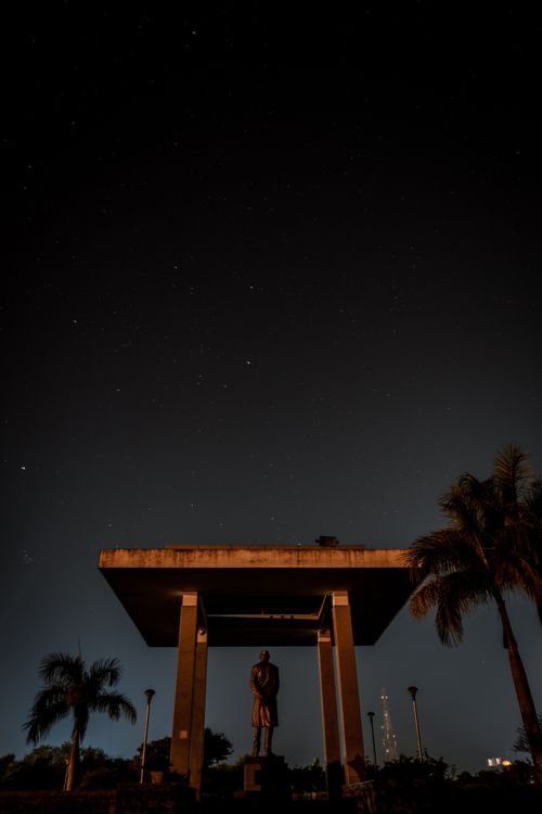 Free Silhouetted statue under starry sky with palm trees and modern structure. Stock Photo