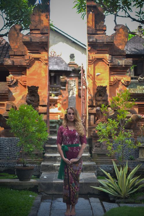 Free A woman in traditional dress stands at the entrance of a historic temple, surrounded by lush greenery. Stock Photo