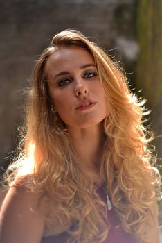 Elegant portrait of a blonde woman with wavy hair in natural sunlight.
