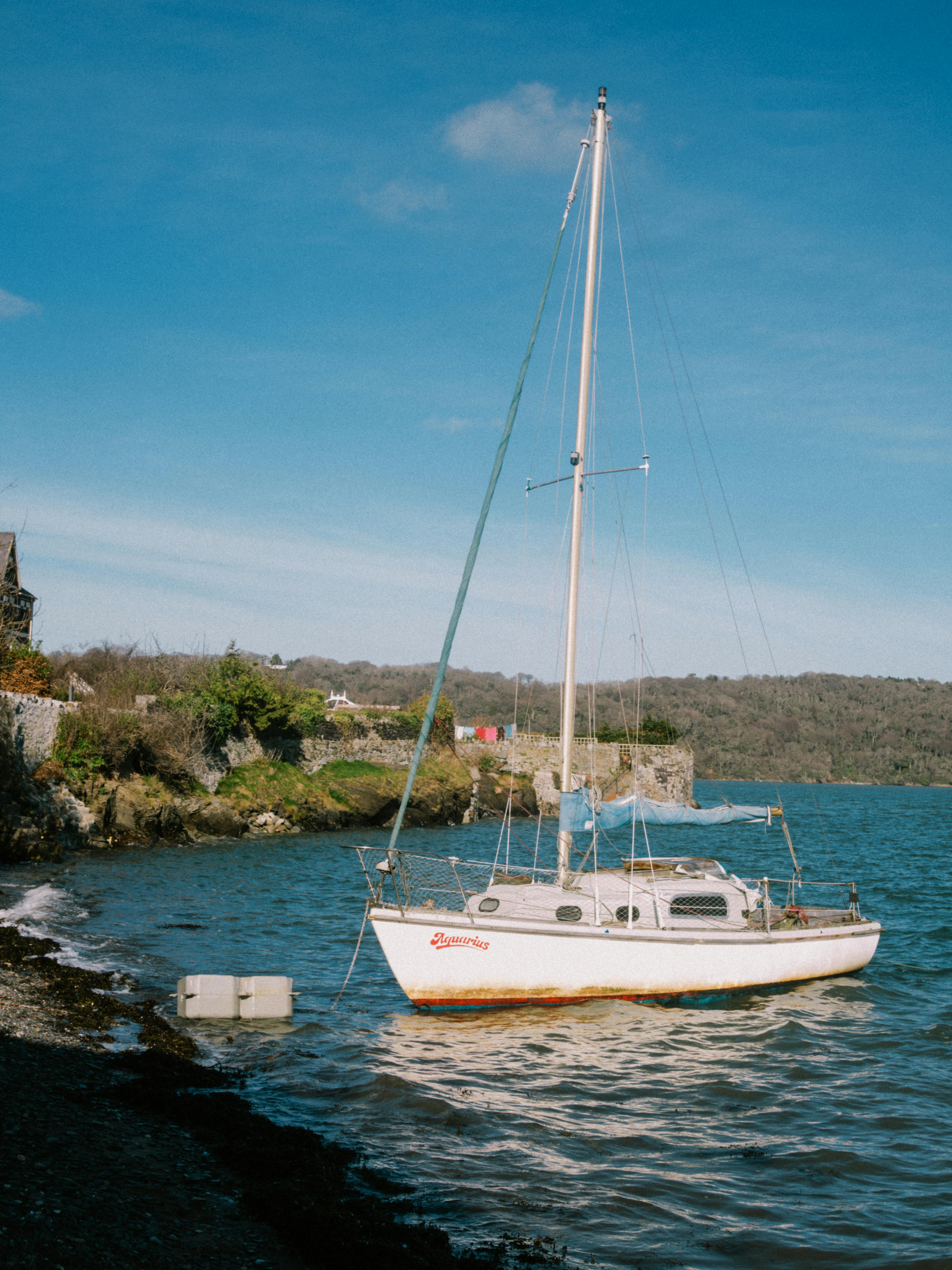 A serene view of a sailboat anchored by Bangor's rocky coastline under clear blue skies.