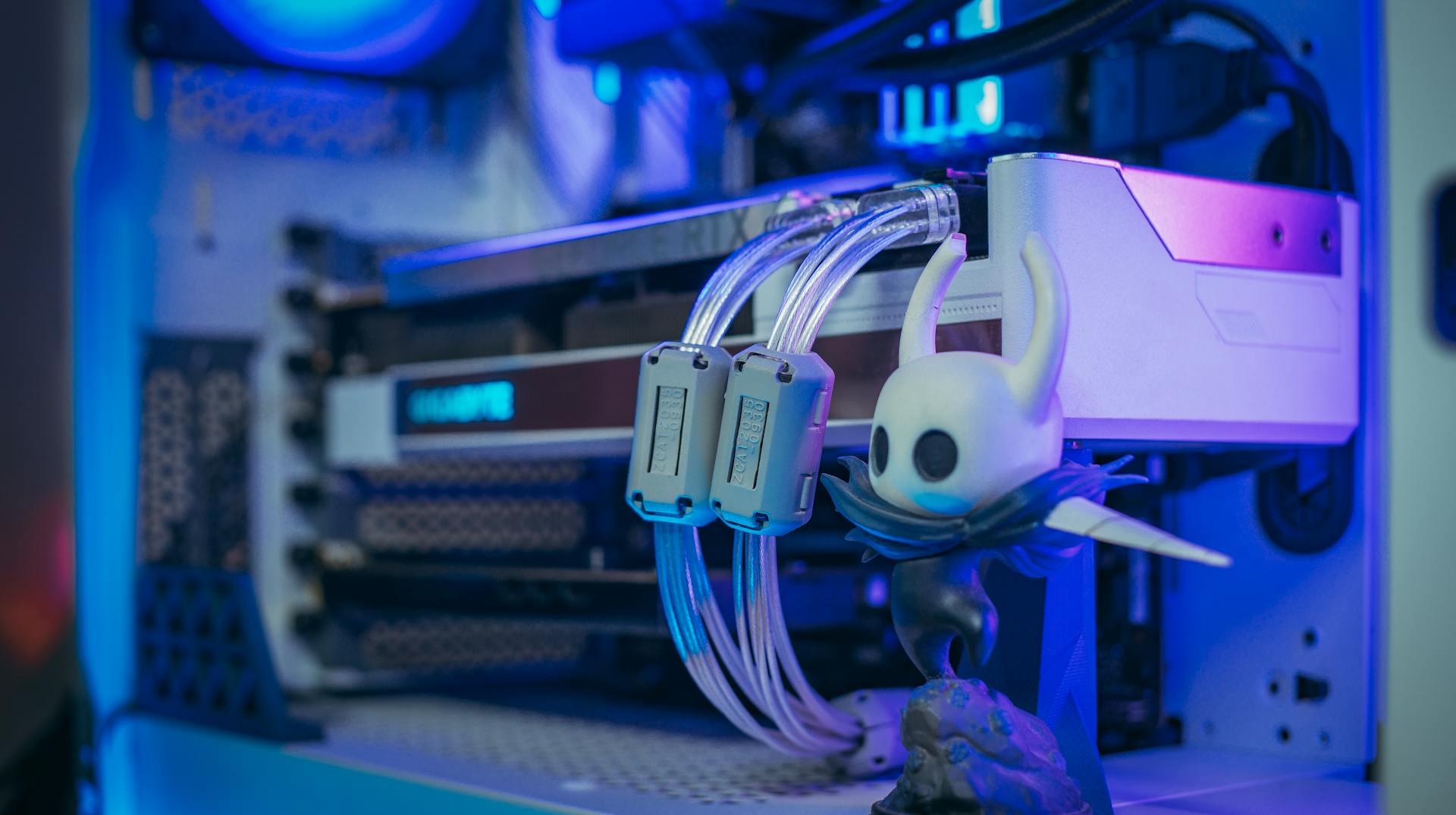 Close-up shot of a custom gaming PC with liquid cooling and figurine under blue lighting.