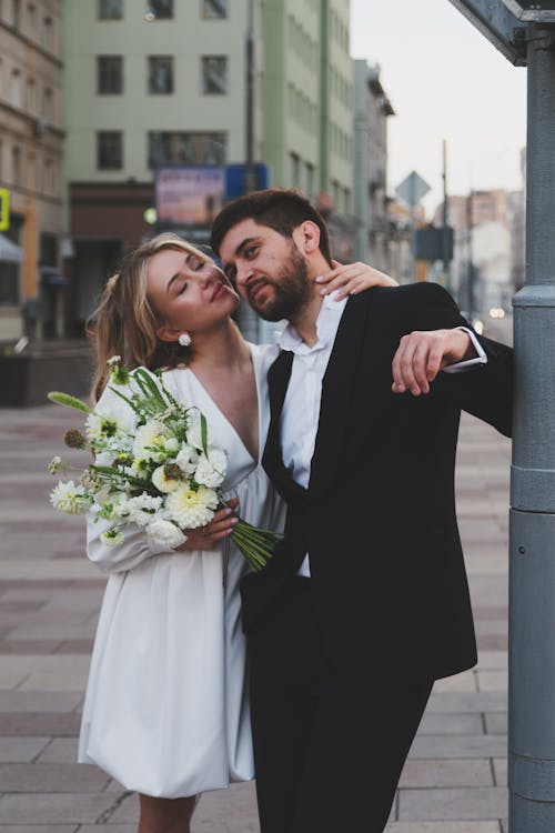 Free Woman in Dress and Man in Suit Kissing on Sidewalk Stock Photo