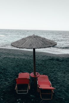 Relaxing view of red beach chairs under an umbrella facing the ocean in Mononaftis, Greece.