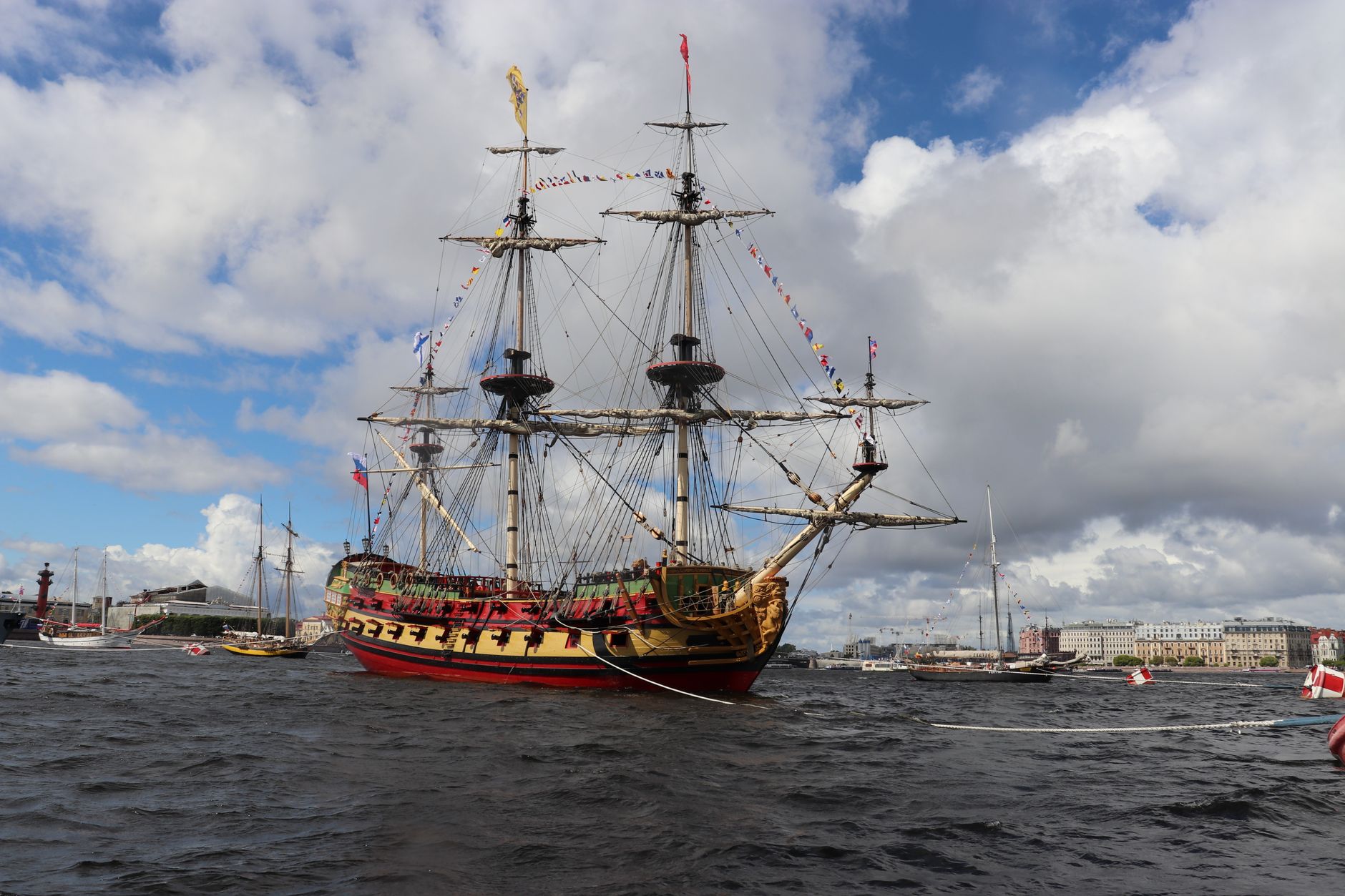 A vintage sailing ship docked in a picturesque harbor with a cloudy sky backdrop.