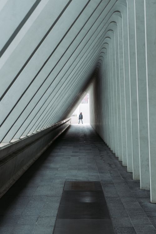 Free Intriguing perspective of a modern architectural hallway with a lone figure at the end. Stock Photo