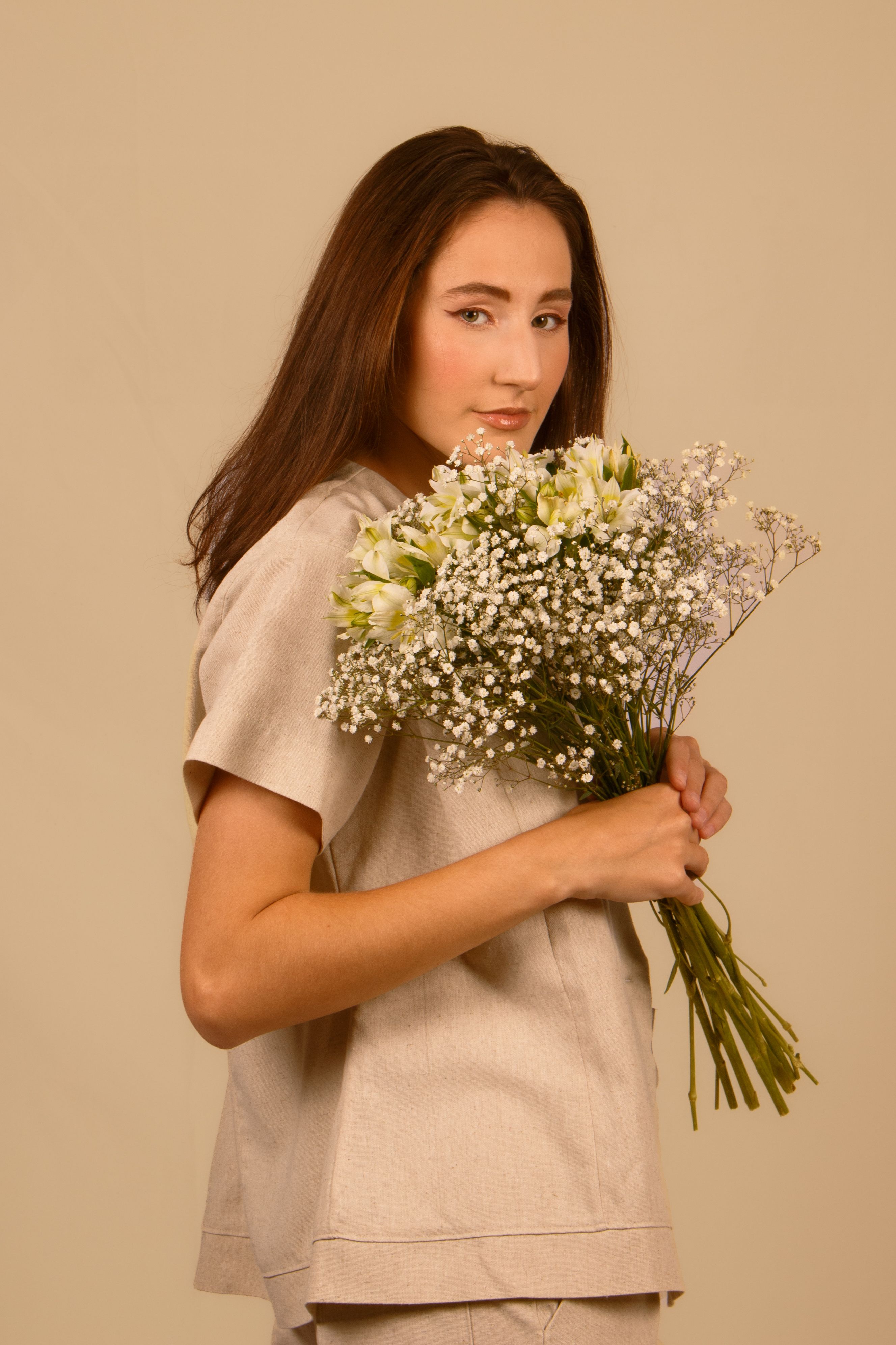 Elegant portrait of a woman with long hair holding a bouquet of white flowers against a soft yellow background.