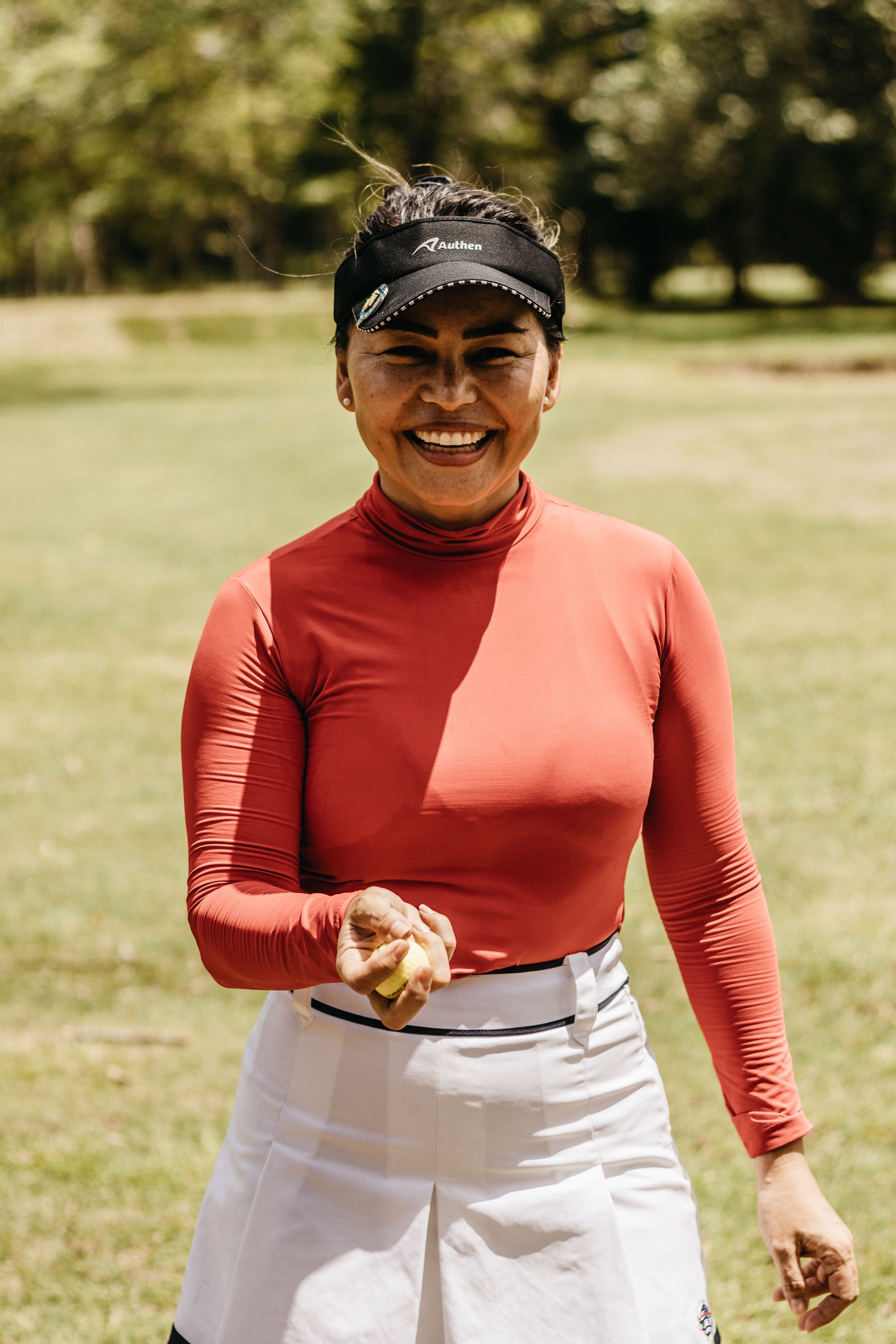 A cheerful woman in sporty attire smiles brightly in a sunny outdoor setting.
