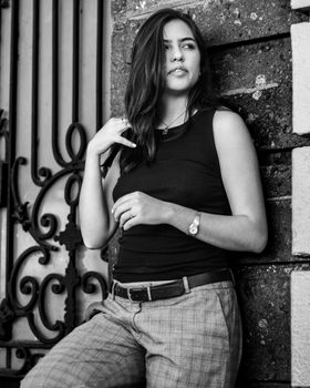Black and white portrait of a fashionable brunette woman leaning against a wall.
