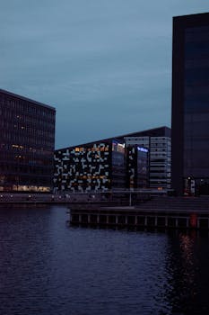 Illuminated modern buildings by a waterfront at dusk, capturing urban architecture.