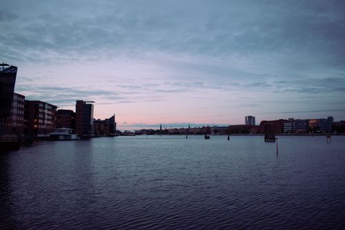 Free Panoramic view of Copenhagen's waterfront skyline at dusk featuring urban buildings and calm sea. Stock Photo
