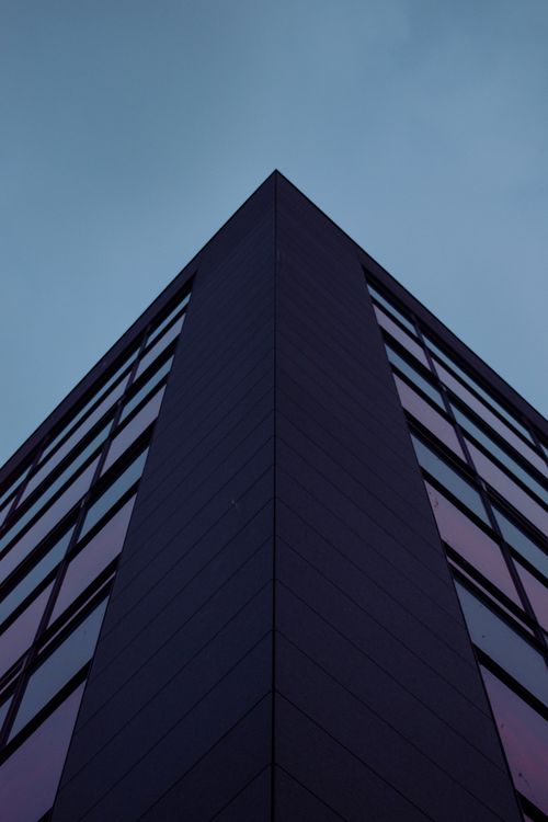 Free A striking upward view of a modern office building corner against a moody evening sky. Stock Photo