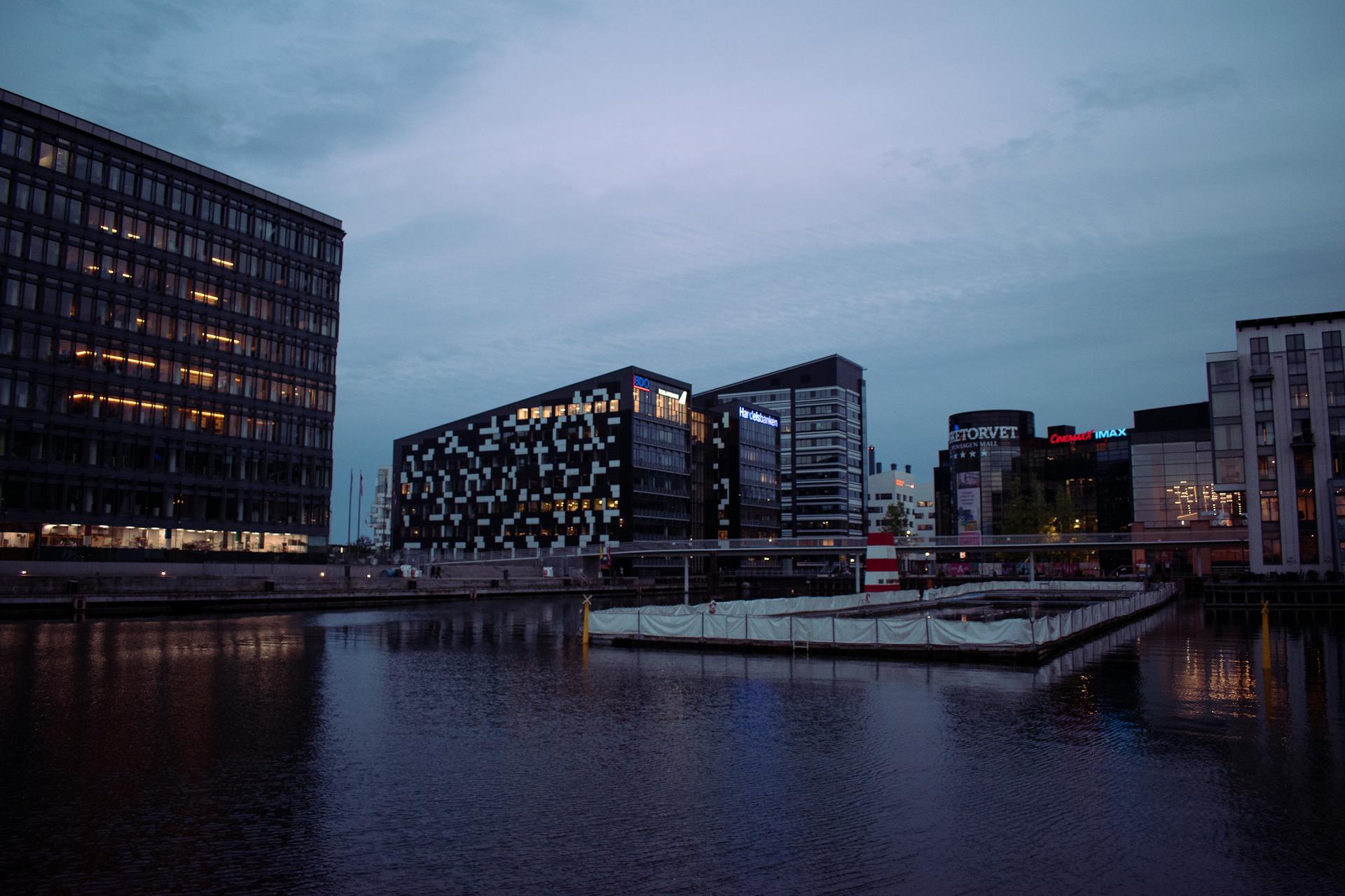 Evening view of modern architecture along Copenhagen harbor, reflecting in calm waters.