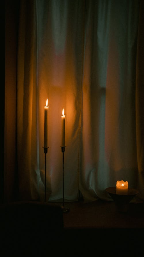 Photo of Lit Candles on a Table next to White Curtains