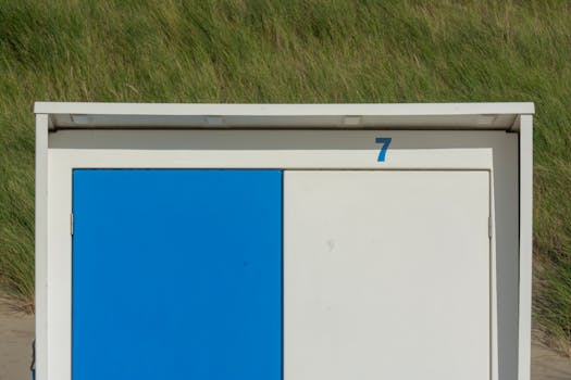 Close-up of a blue and white beach shed numbered seven against a grassy backdrop.