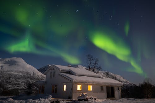 View of Northern Lights above a House and Mountains 