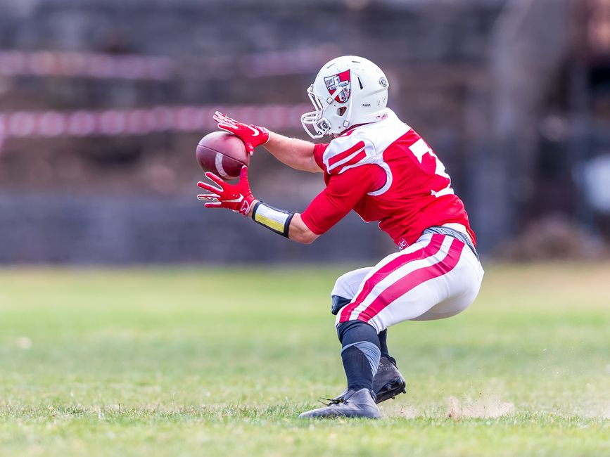 A football player in red uniform dramatically catching a ball on a grassy field during a game.