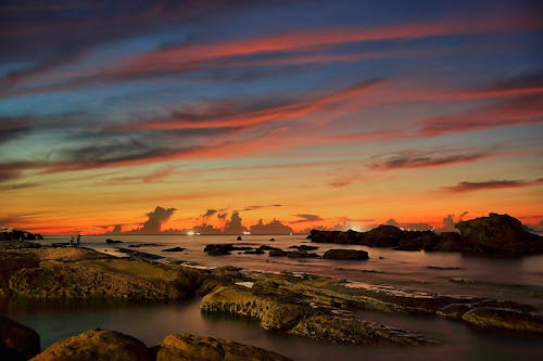 Body of Water Near Rock Formation during Orange Sunset