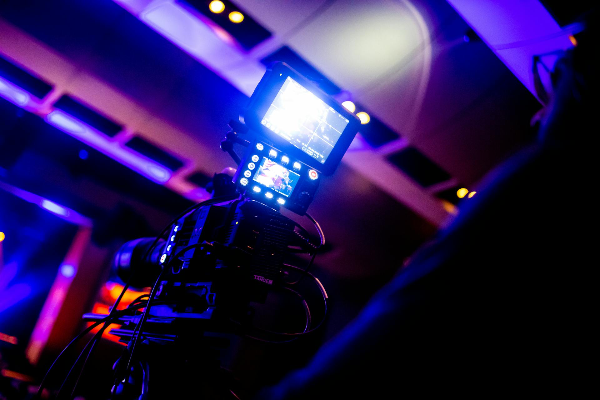 Close-up of a high-tech video camera under vibrant studio lights, perfect for broadcasting and entertainment.