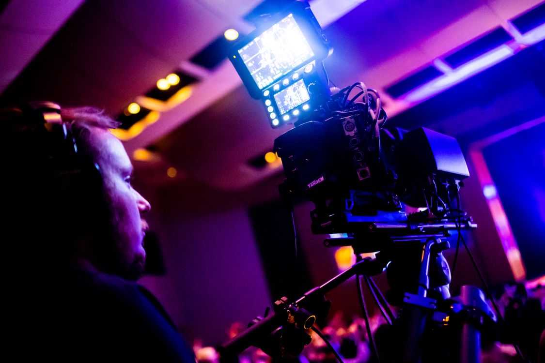 Free A professional cameraman operating a camera during a vibrant nightlife event indoors. Stock Photo
