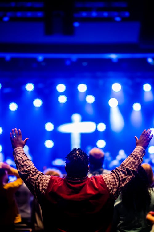 Photo of a Man Raising his Hands towards a Stage with a Cross