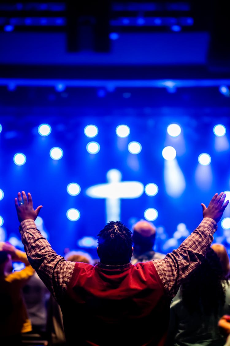 Photo Of A Man Raising His Hands Towards A Stage With A Cross