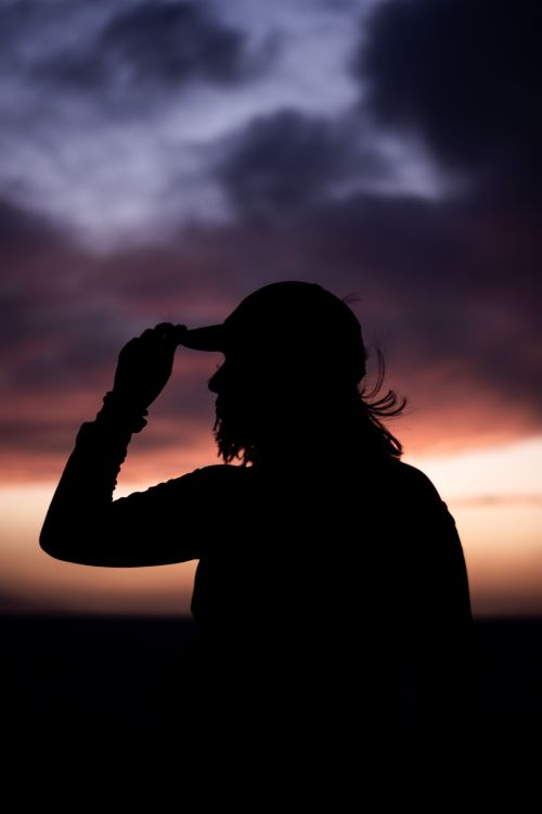 Free Dramatic silhouette of a man with a cap against a vibrant sunset sky, creating a mysterious mood. Stock Photo