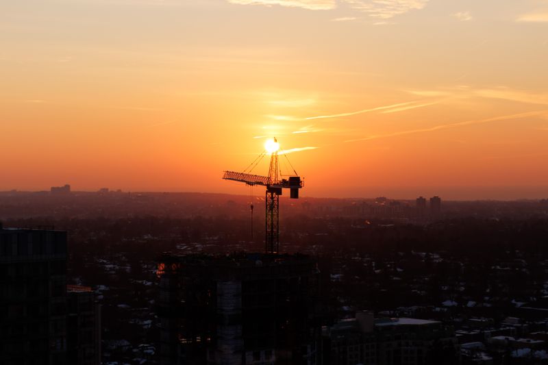Silhouette of a construction crane against a colorful urban sunset.