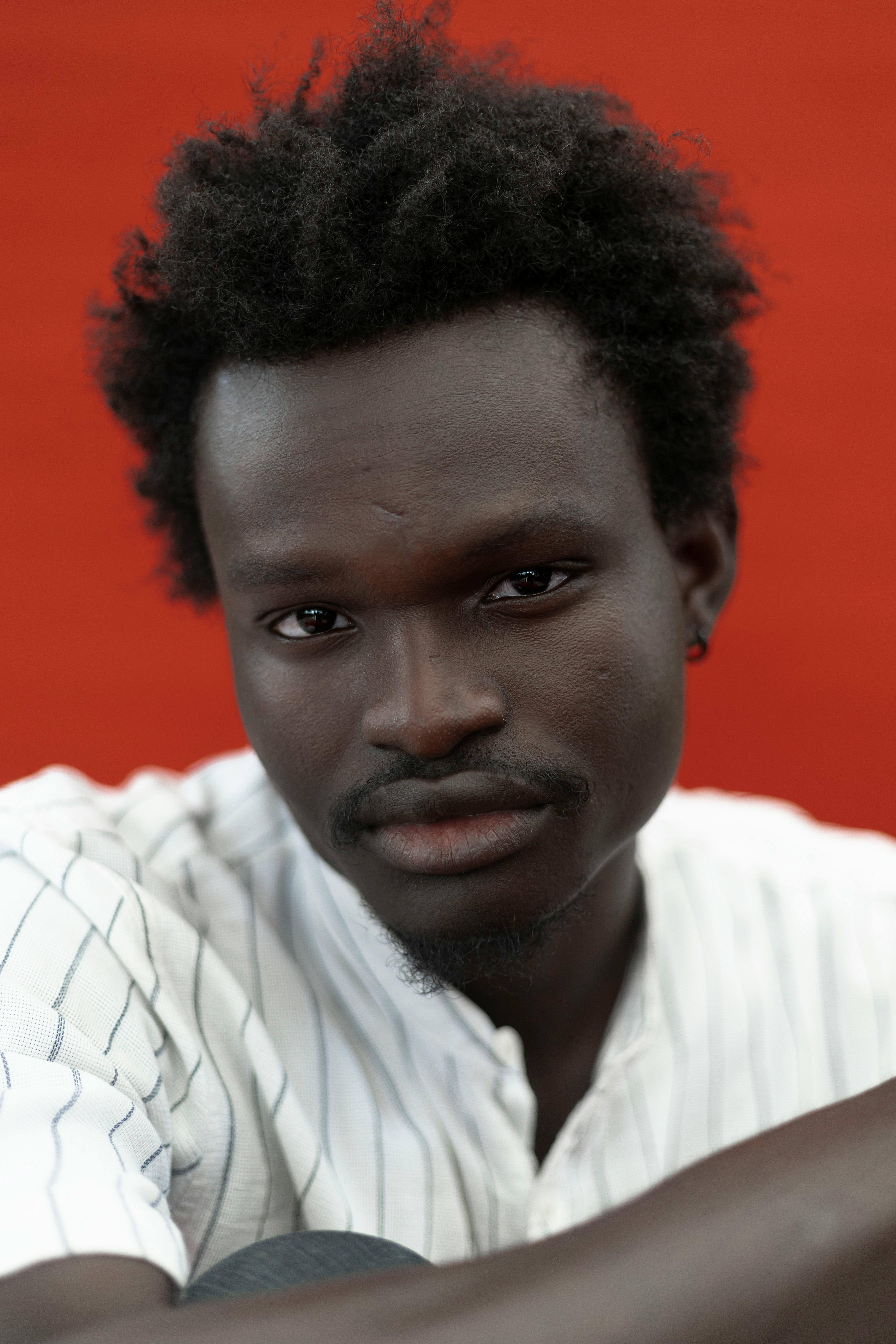Close-up portrait of a man with an afro hairstyle against a vibrant red background.