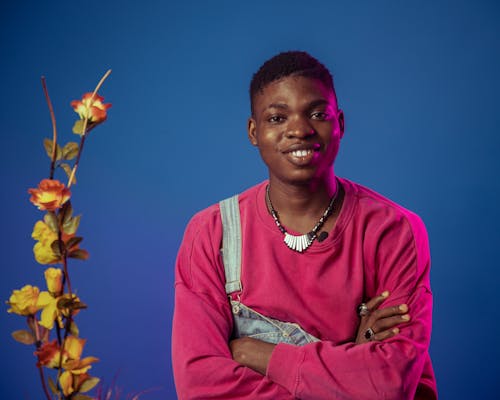 Young Man in a Pink Blouse and Denim Overalls Posing in Studio on Blue Background 