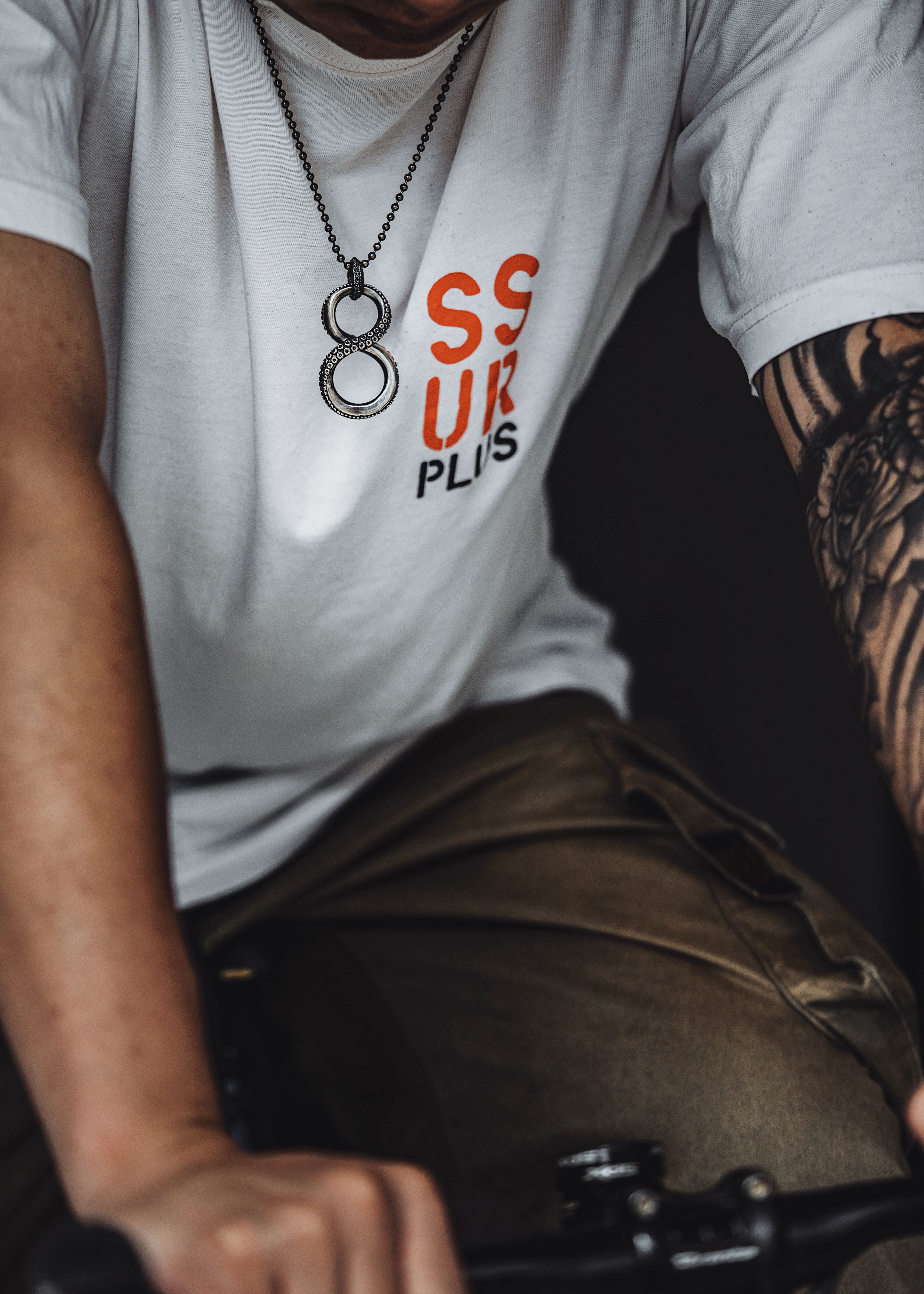 Close-up of a tattooed man in a white T-shirt on a bicycle indoors.