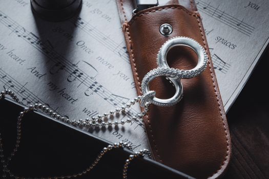 Elegant silver pendant lying on leather case over sheet music background.