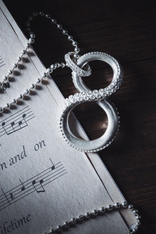 Free A silver infinity necklace elegantly draped over sheet music, capturing the essence of timeless elegance. Stock Photo