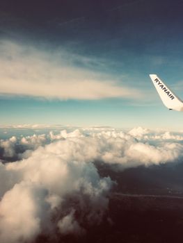 Wing of an airplane flying above fluffy clouds with a clear sky in the background.
