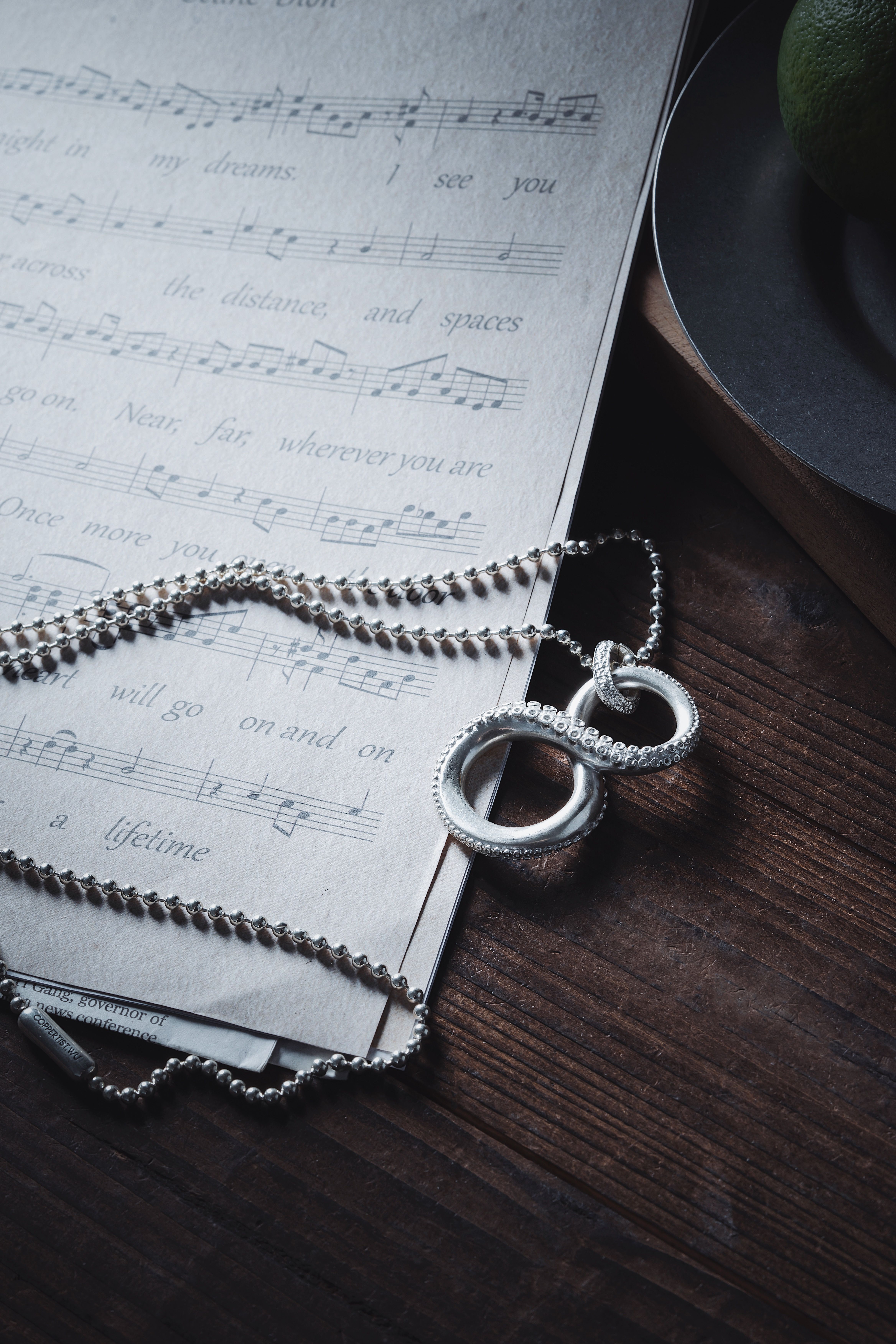 Artistic shot of a silver necklace resting on musical sheet, evoking a vintage and dramatic feel.
