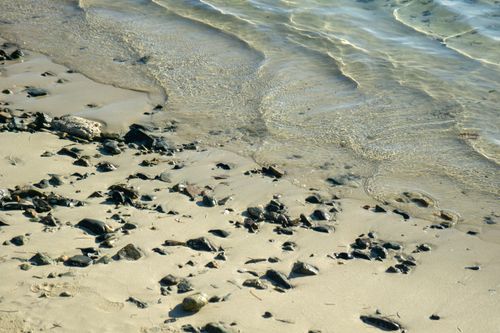 Free A tranquil beach scene with small rocks scattered on the sandy shore and gentle waves. Stock Photo